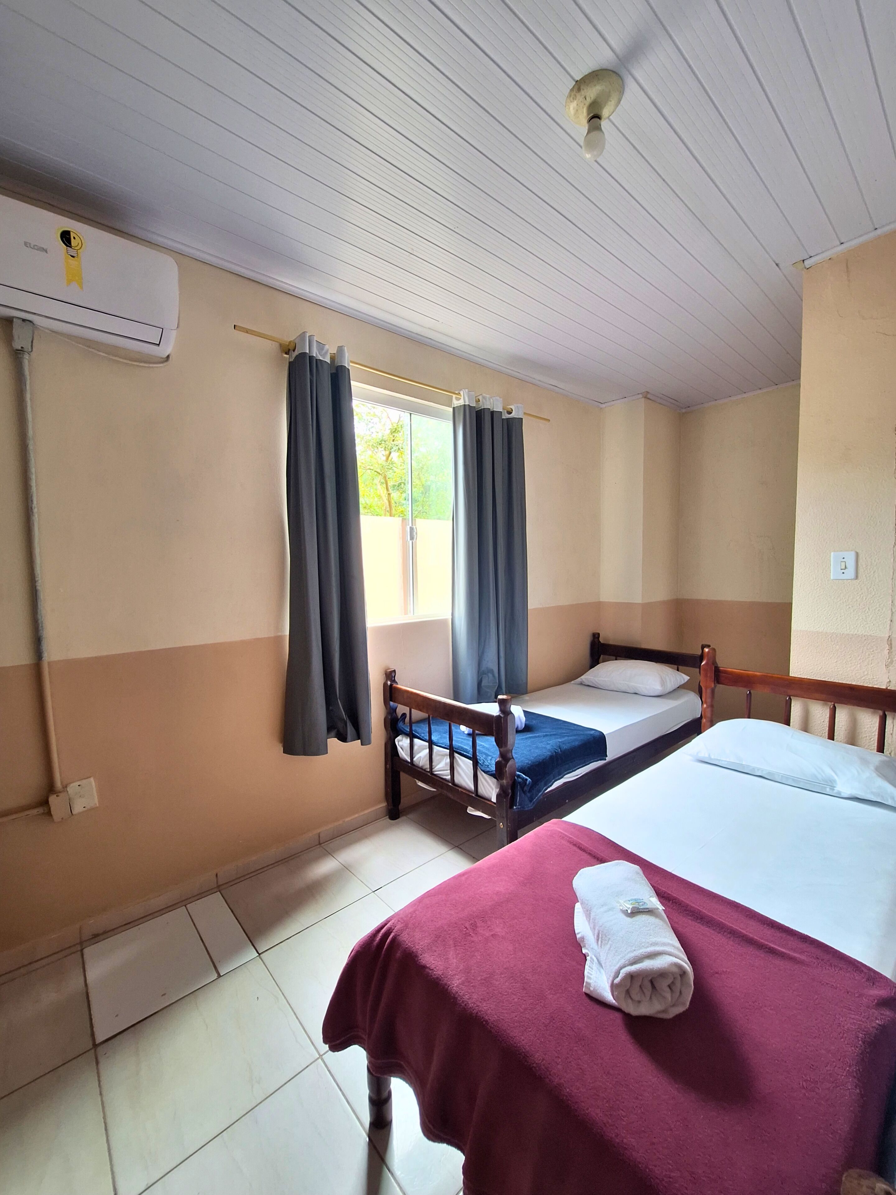 Een kamer met twee bedden, een raam met gordijnen, een plafondventilator en een airconditioning.