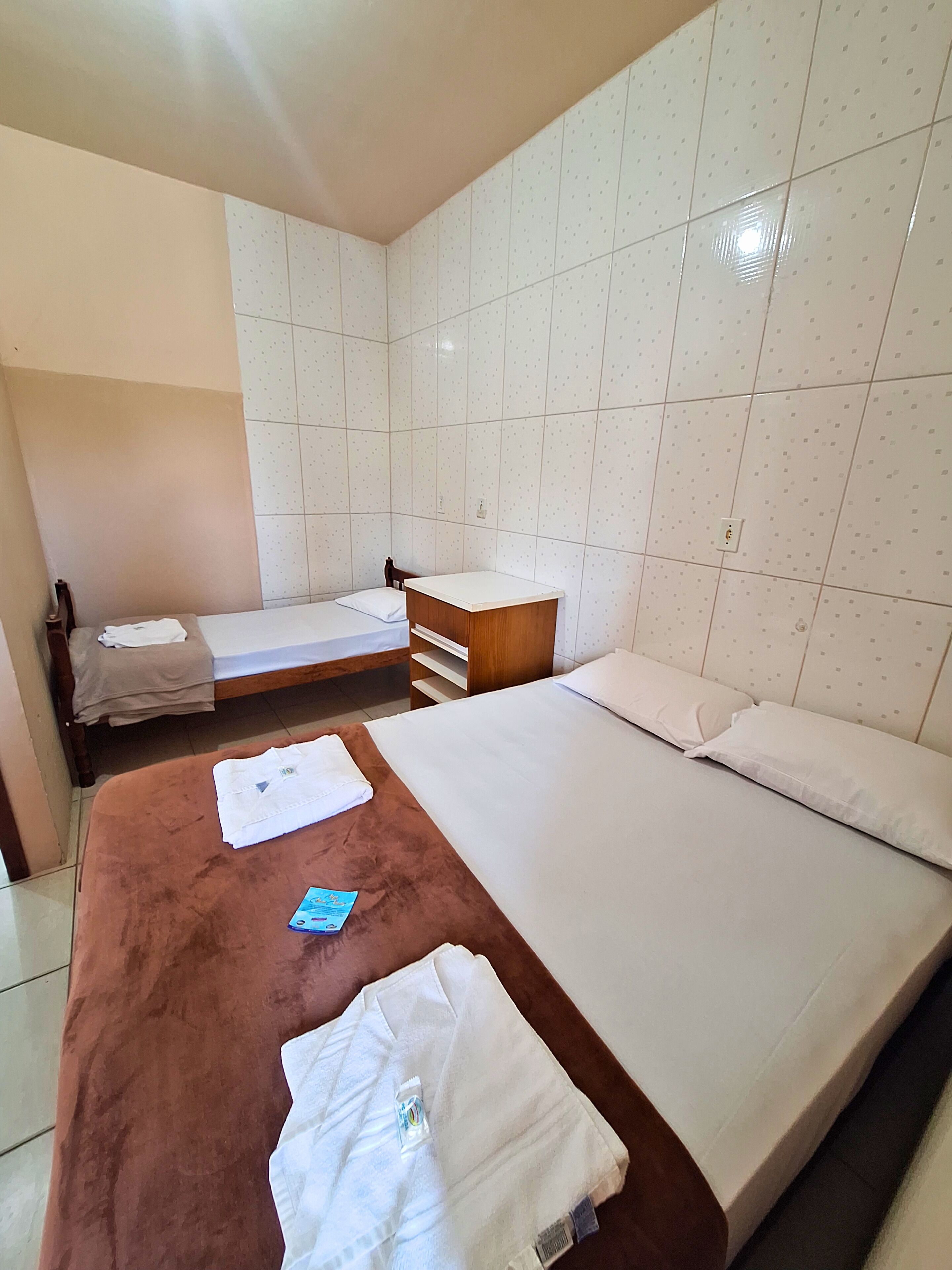 Une chambre d’hôtel avec deux lits, une table de chevet en bois, un mur recouvert de carreaux et une moquette marron.