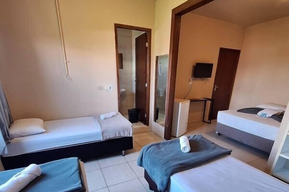 A hotel room with two beds, a small table, a TV, and a shower area.