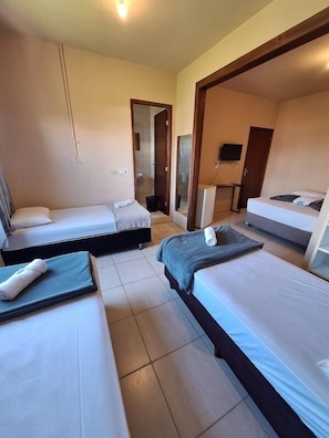 Quarto de hotel com três camas, uma televisão e uma porta para o banheiro.