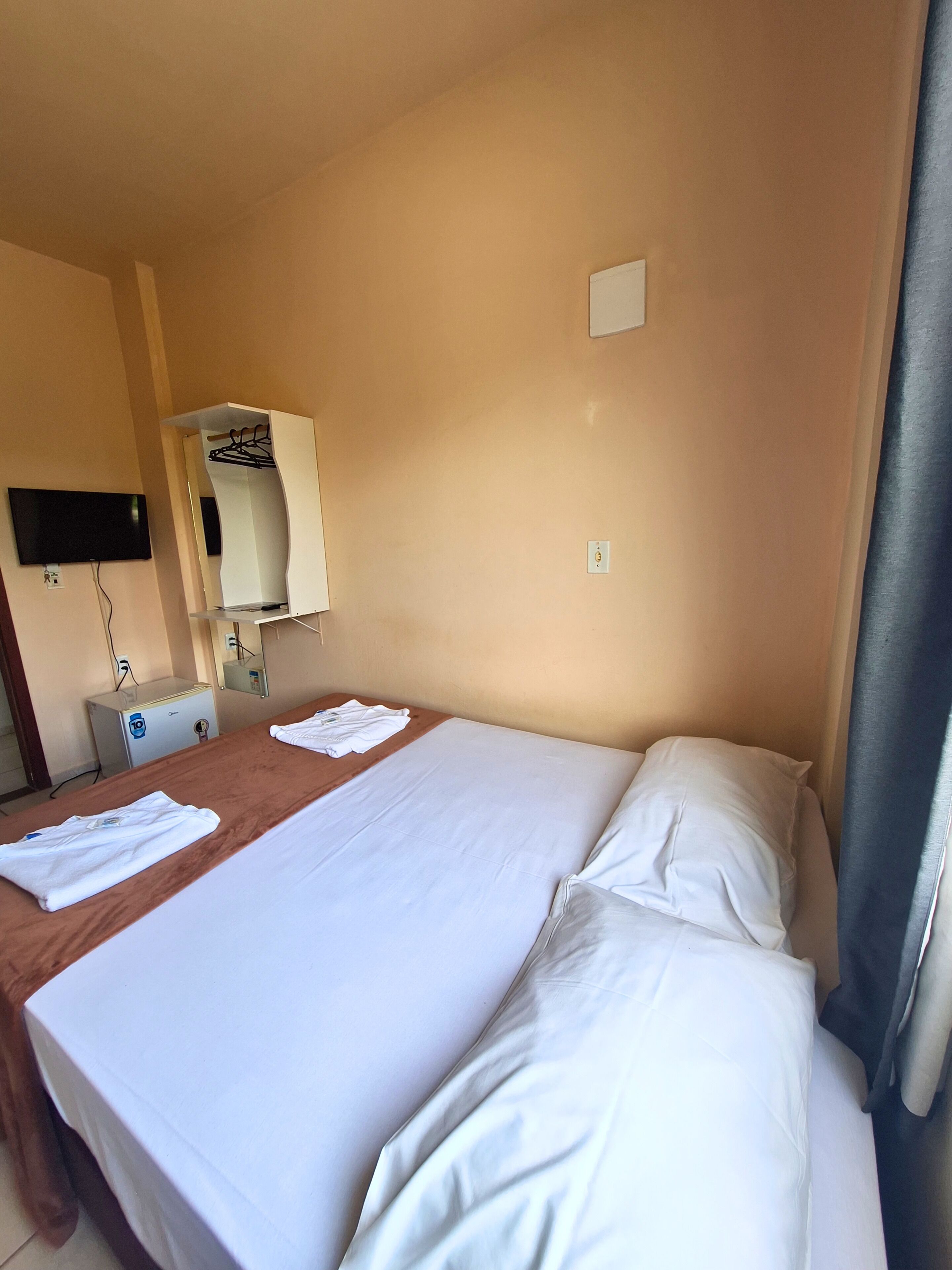 Una camera d'albergo con un letto, una scrivania, una televisione a schermo piatto e un piccolo frigorifero.