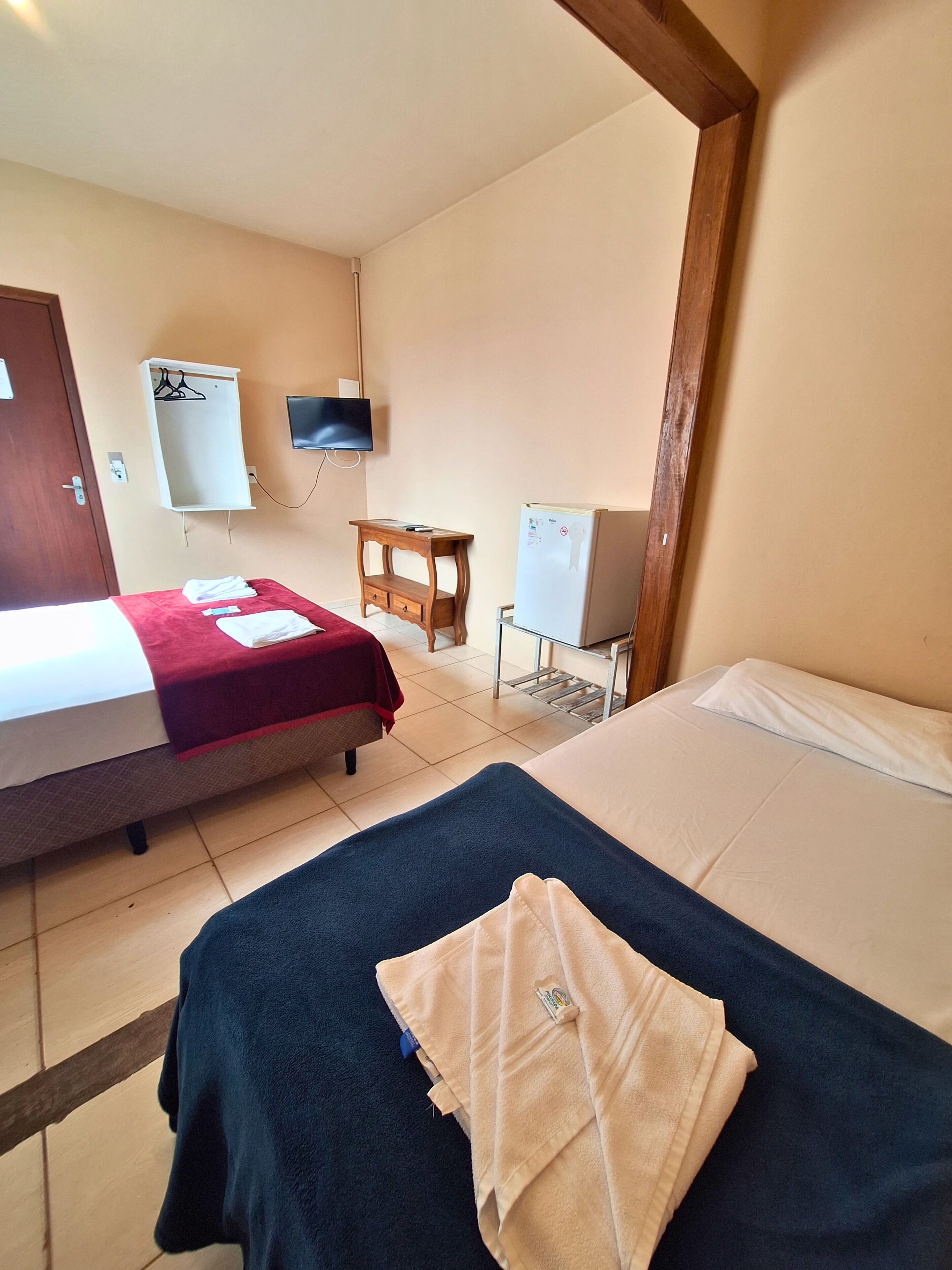 Una habitación de hotel con dos camas, televisión, una mesita y un refrigerador.