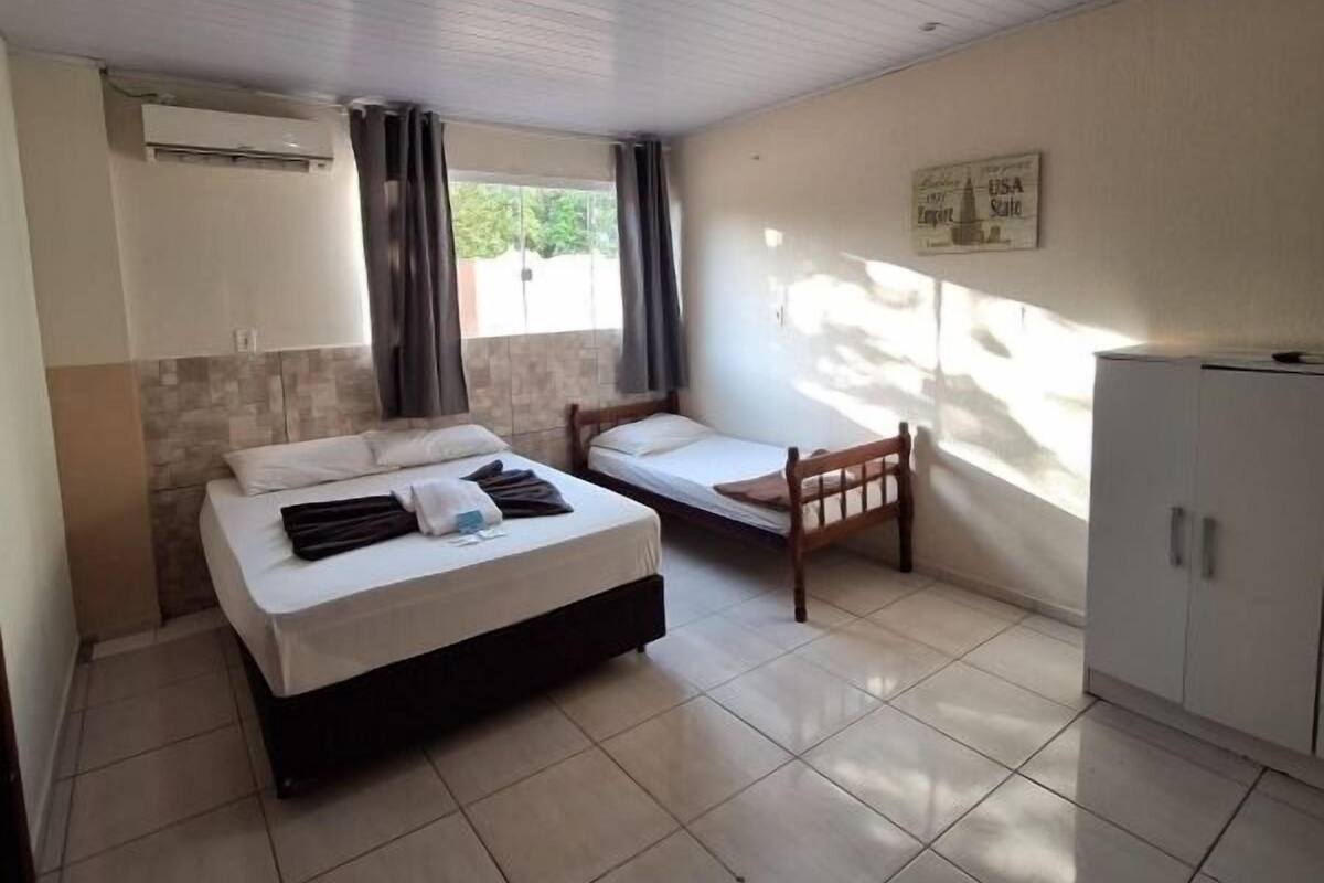 A bedroom with a bed, a smaller bed, a chair, a wardrobe, and a window with curtains.