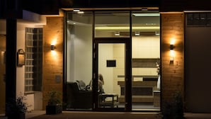 A hotel entrance at night with illuminated signage, a glass door, and a visible interior with seating. - River Lodge (Vienna)