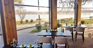 An outdoor dining area with tables and chairs, a view of a lake, and a wooden deck. - River Lodge (Vienna)