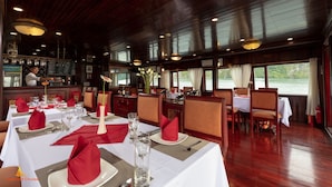 Un restaurante con mesas dispuestas para comer, una zona de bar y amplios ventanales con vista al agua.