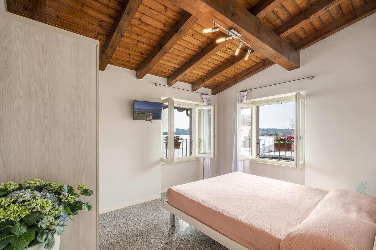 Ein Schlafzimmer mit Holzboden, einem Bett, einer Topfpflanze und Blick auf einen Balkon mit Blumen.