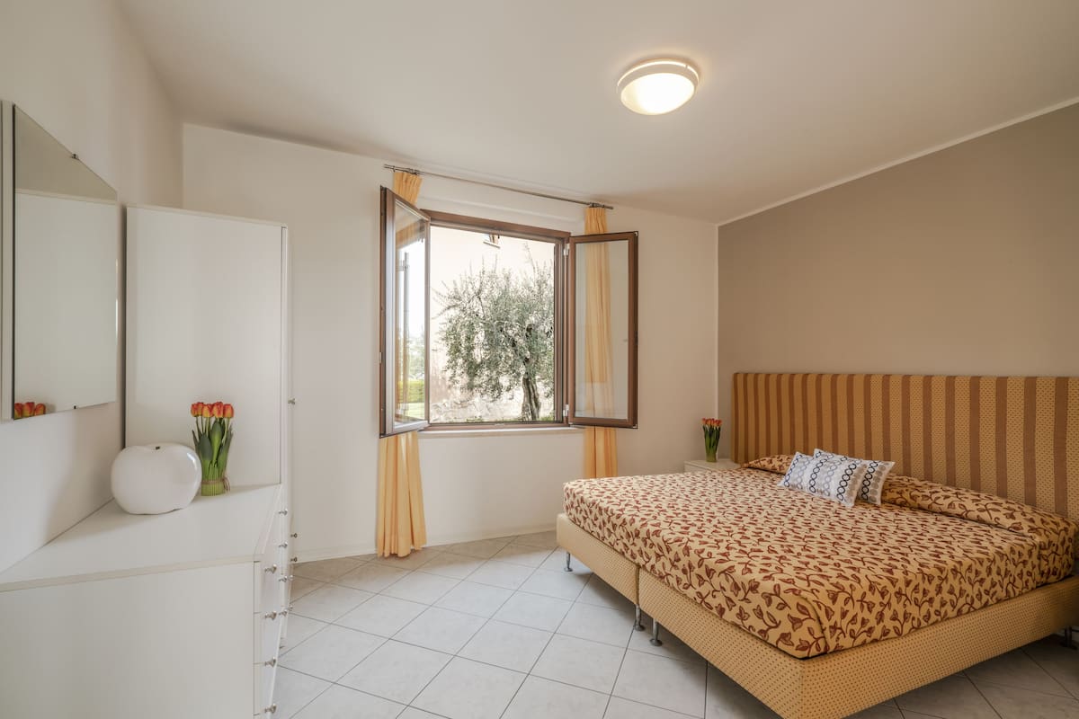Ein Schlafzimmer mit Bett, Schminktisch, Spiegel und einem fenster mit Vorhängen.