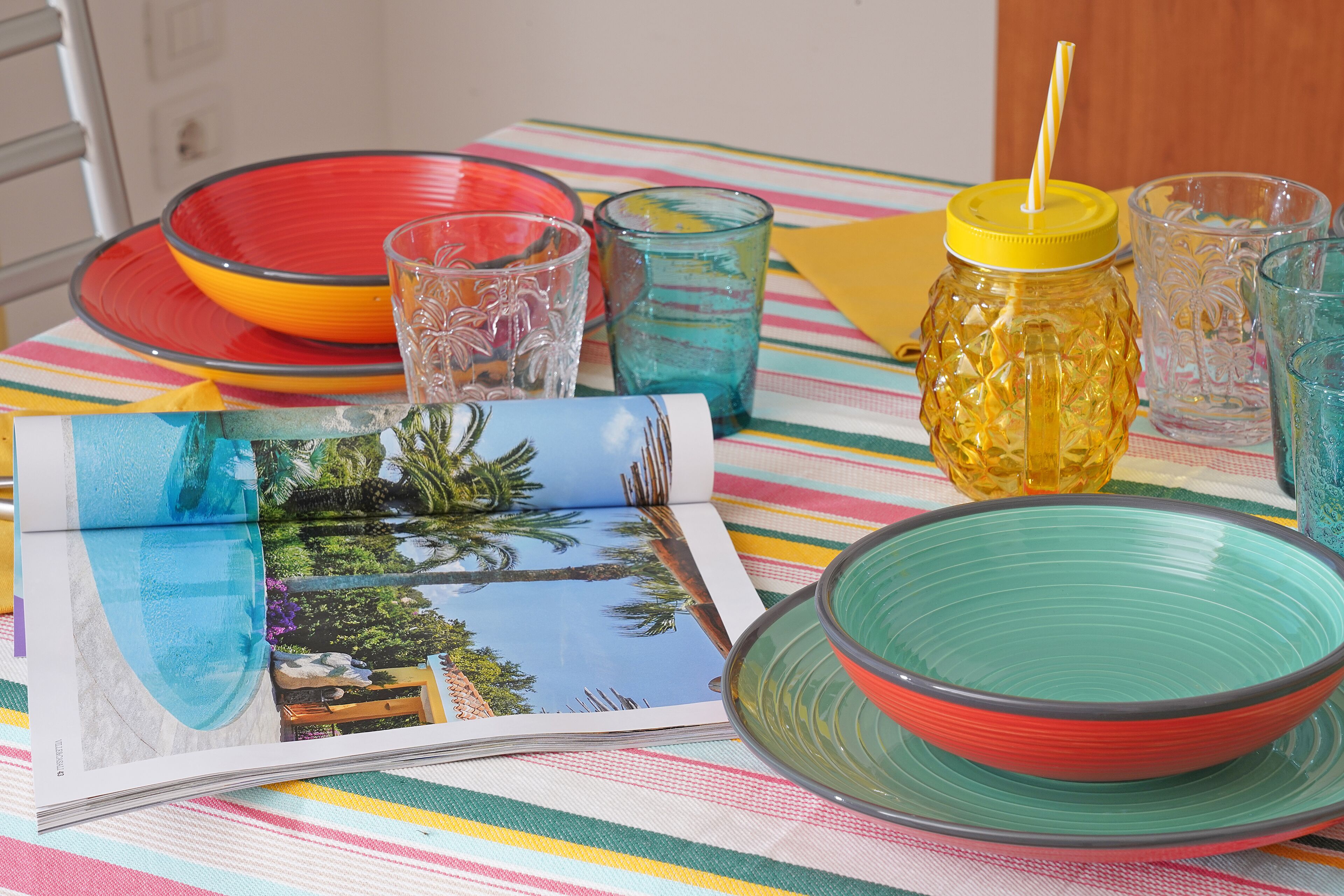 A table with colorful plates, glasses, and a magazine featuring a tropical scene.