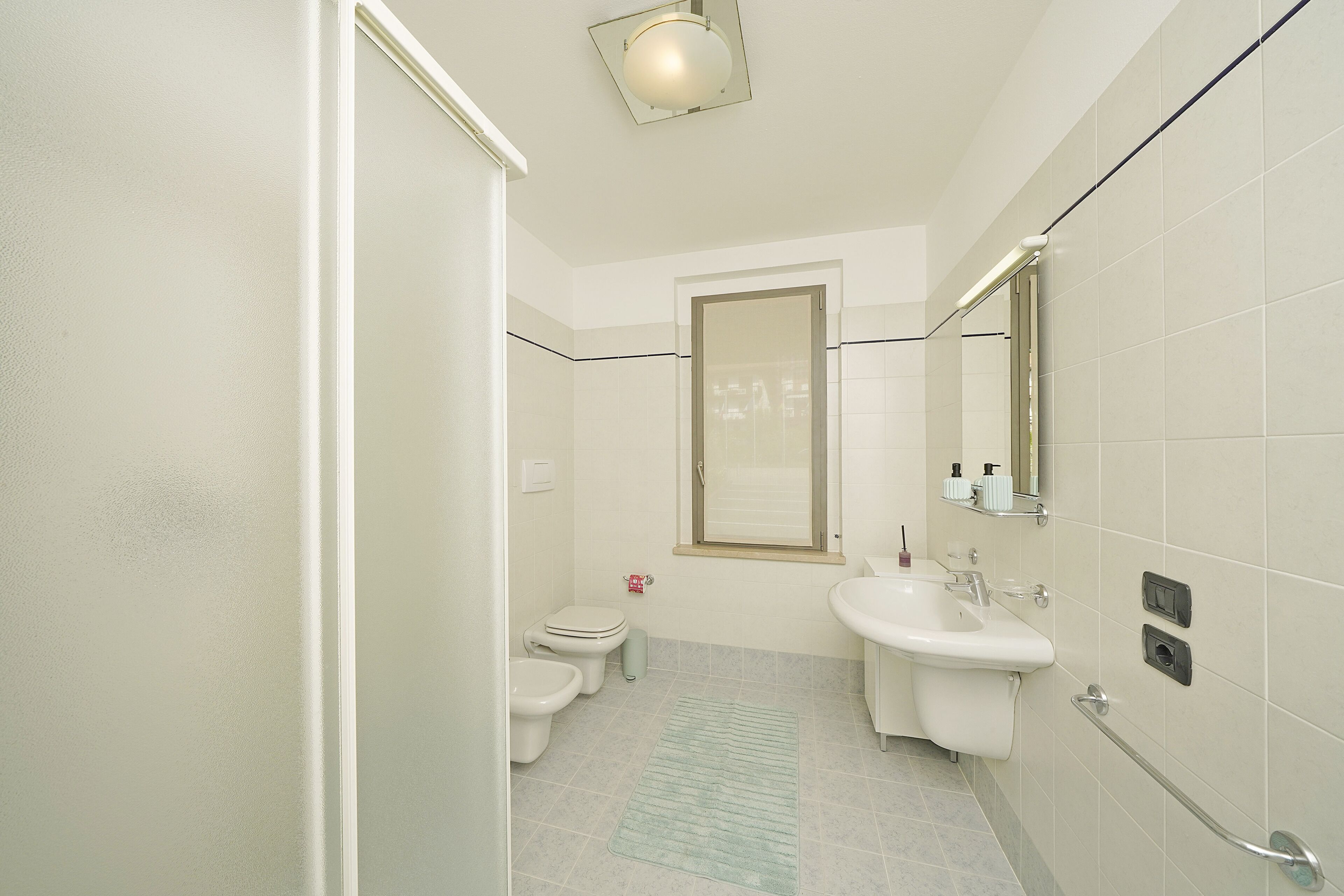 A bathroom with a toilet, bidet, sink, and a handrail.