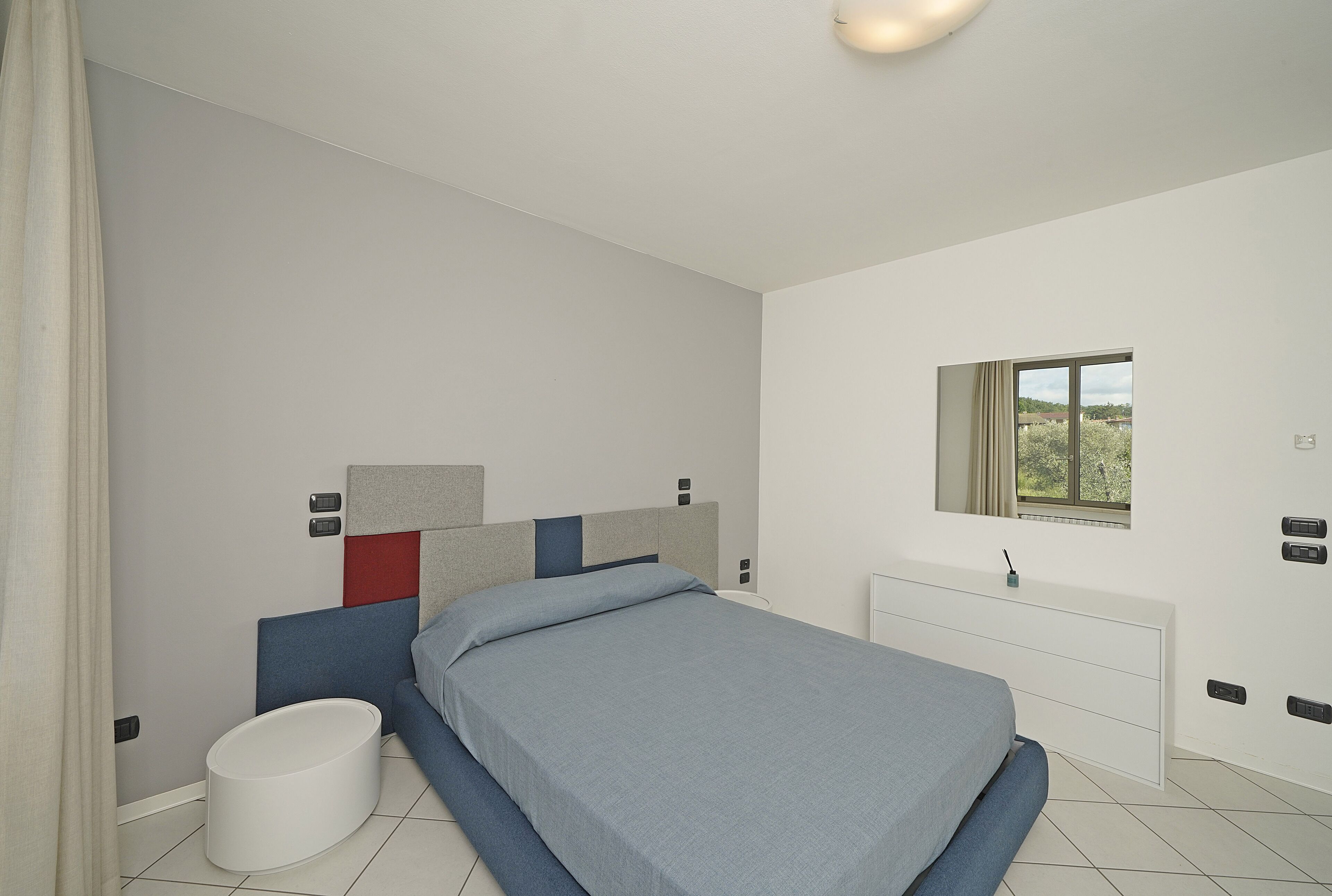 A modern bedroom with a bed, bedside table, and a window.