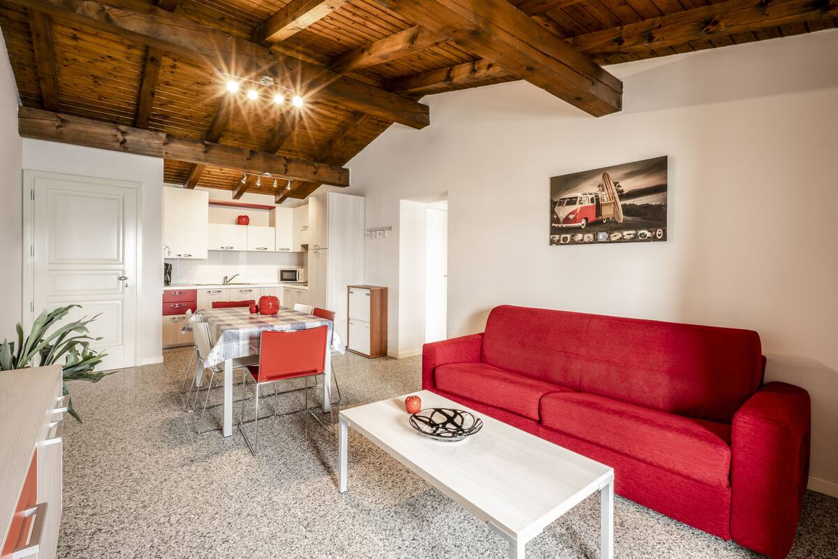 Ein Wohnzimmer mit einem roten Sofa, einem weißen Couchtisch und einer Küche im Hintergrund.