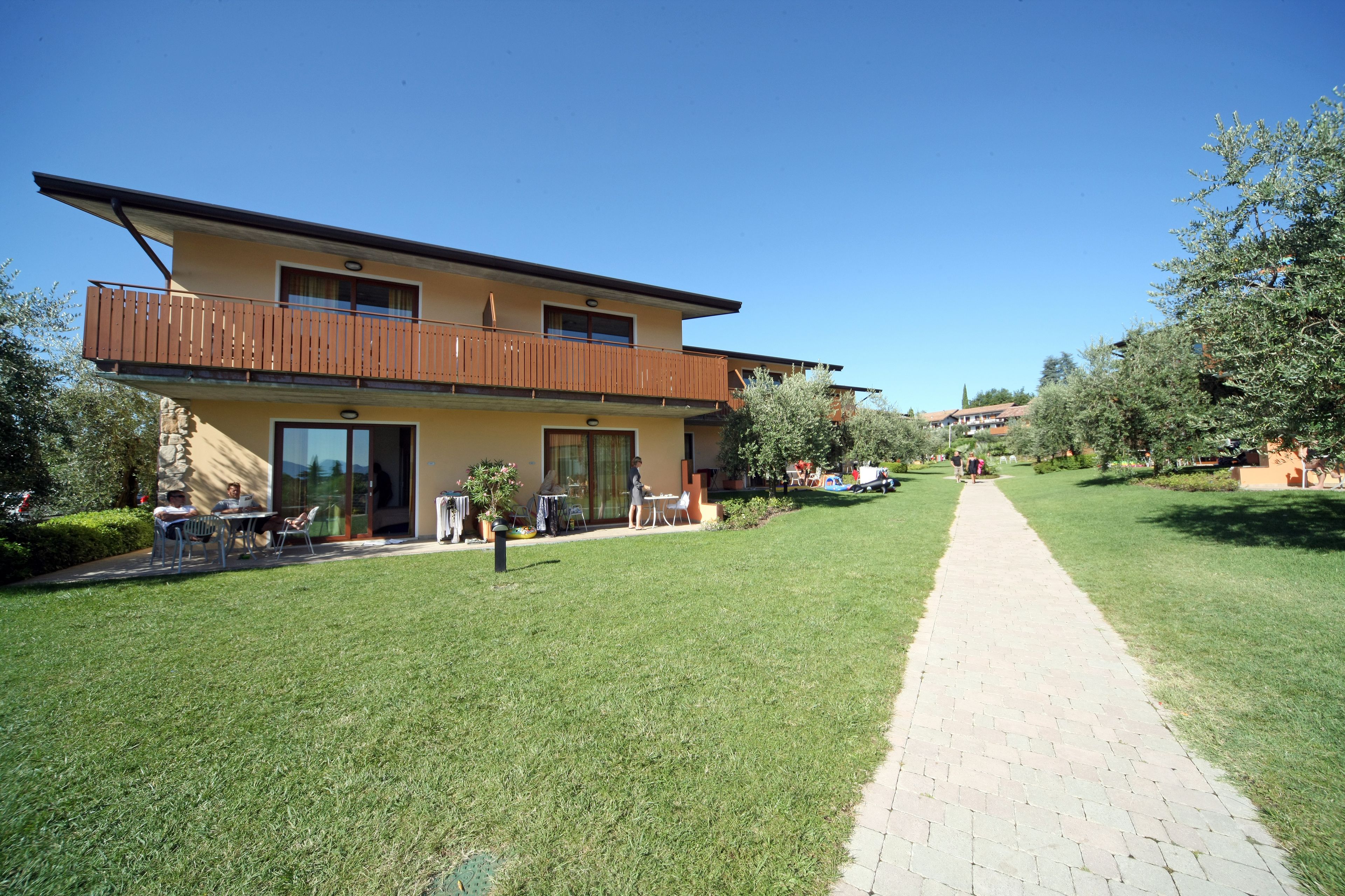 A two-story building with a balcony, a paved pathway, and a well-maintained lawn.
