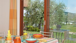 Une table à manger ornée d’assiettes et de verres aux couleurs vives, le tout se détachant sur un décor composé d’arbres et d’un ciel dégagé.