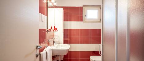 Un baño con un lavamanos blanco, azulejos rojos, un inodoro blanco y una ventana sobre el inodoro.