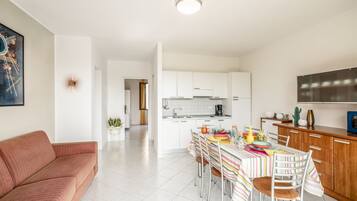 A modern kitchen with white cabinets, a dining table with colorful tablecloth, and a red sofa in the living area.