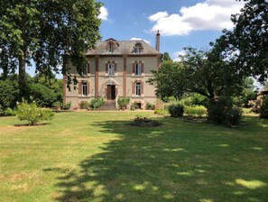 A large, two-story house with a symmetrical facade, a central entrance with steps, and a well-maintained lawn with trees and shrubs. - Domaine Des Trois Chênes (Saint-Jean-Froidmentel)