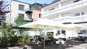 An outdoor patio with tables and chairs, surrounded by buildings. - Hotel zur Post (Brilon)