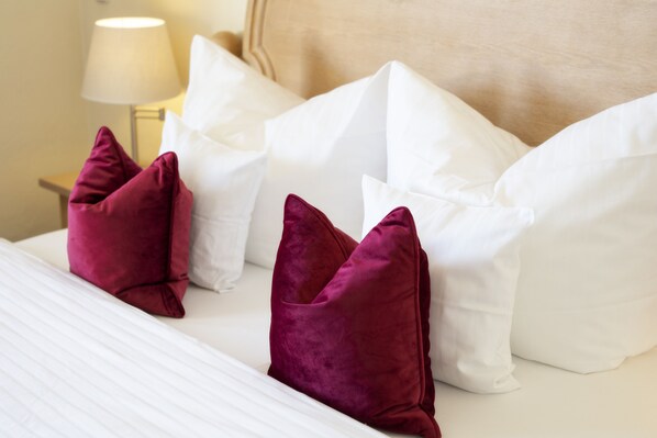 A neatly made bed with white and maroon pillows, a lamp on a bedside table, and a beige headboard.