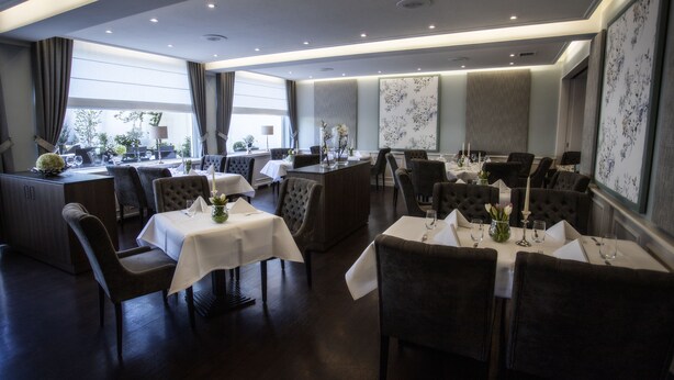 A restaurant with multiple tables and chairs, a bar area, and large windows with curtains. - Hotel zur Post (Brilon)
