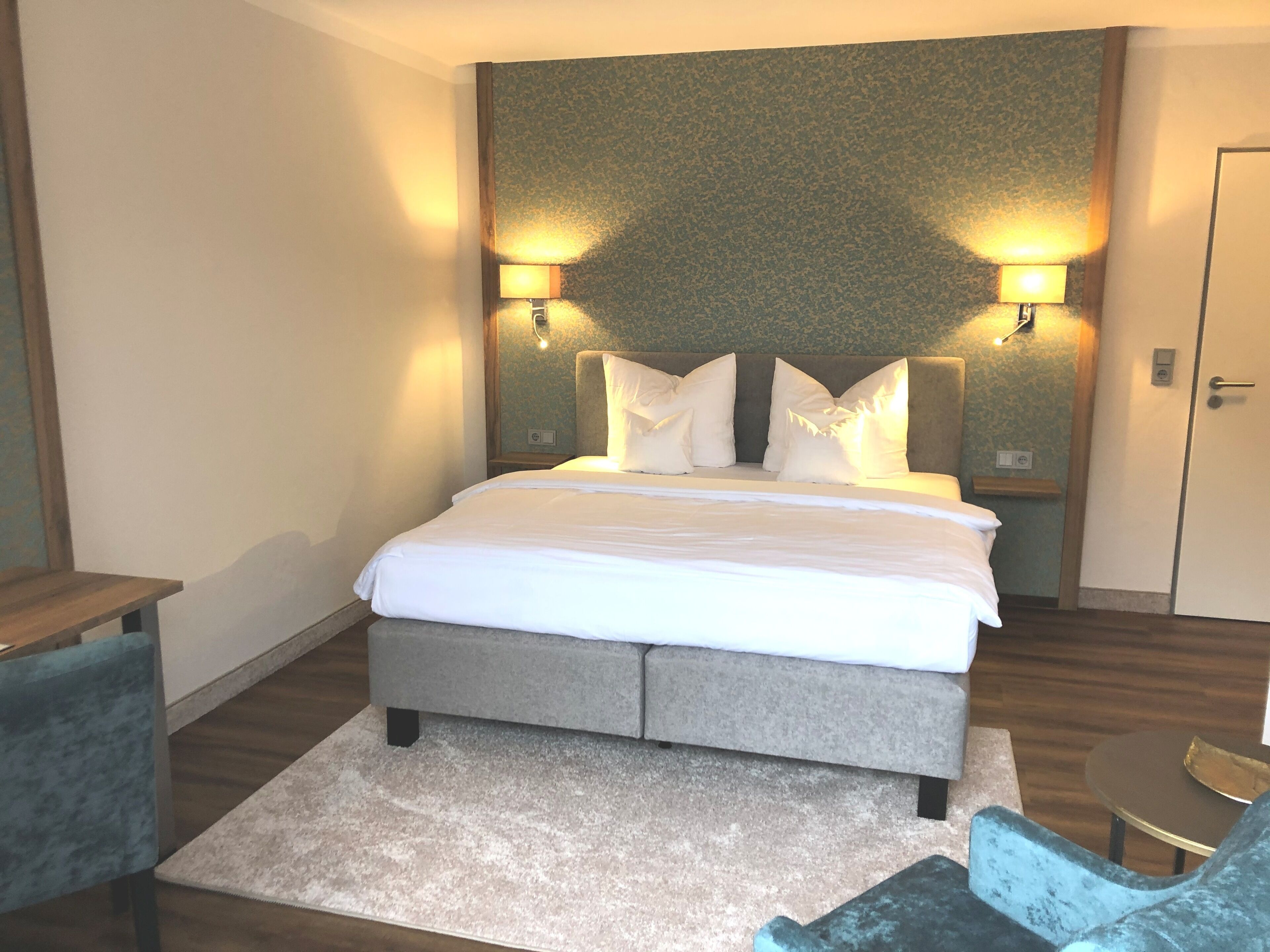 A hotel room with a large bed, two bedside lamps, a small table, and a chair.