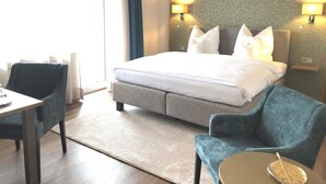 A hotel room with a bed, two armchairs, a small table, and a window with curtains. - Hotel zur Post (Brilon)