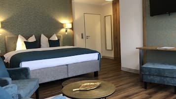 A modern hotel room with a large bed, two armchairs, a small round table, and a TV mounted on the wall.