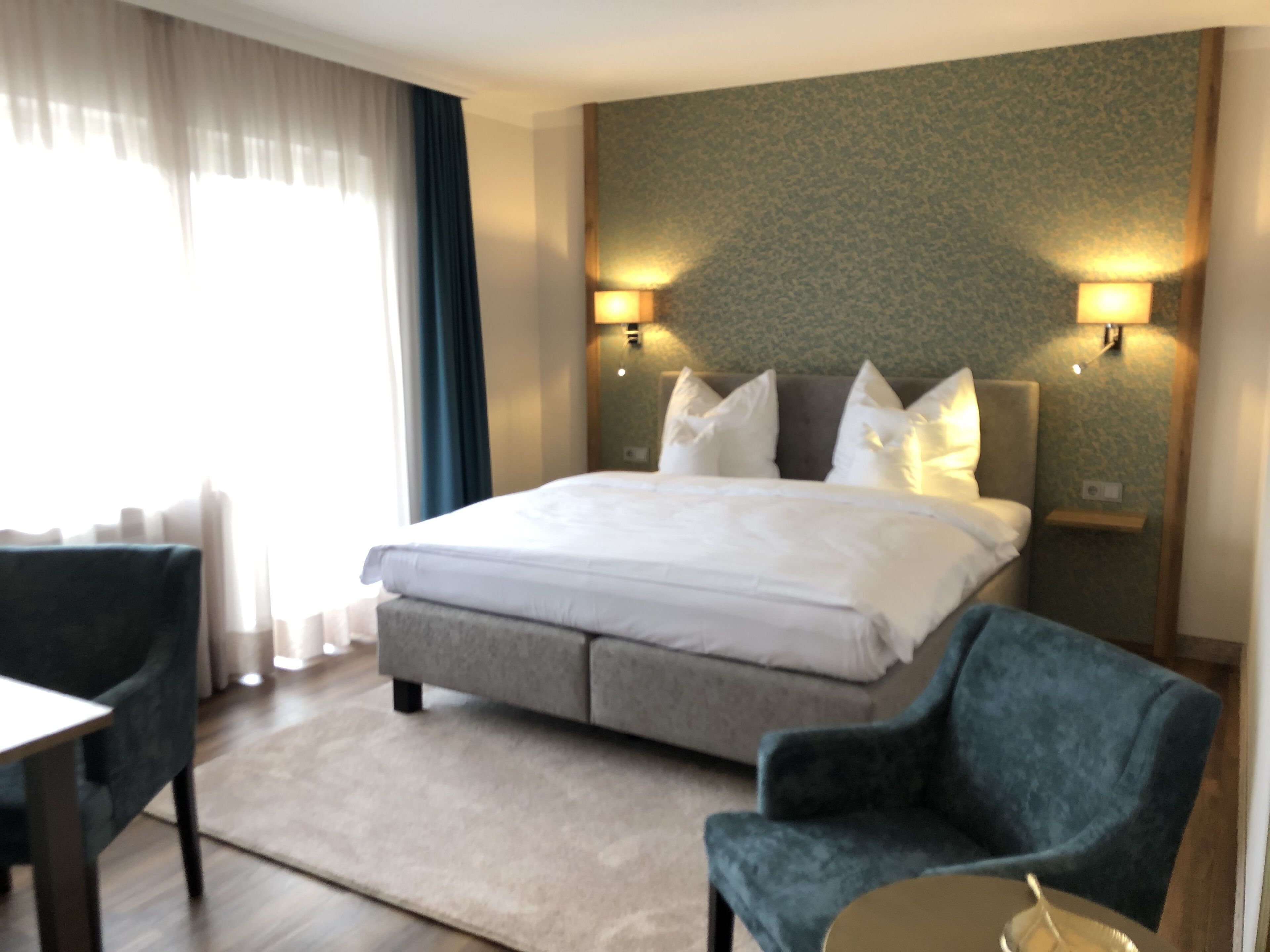 A hotel room with a large bed, two bedside lamps, a grey headboard, a blue armchair, and a small table.