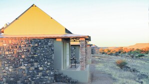 A stone building with a pyramid-shaped roof, a small porch, and a view of a dry landscape. - Alte Kalkofen Lodge (Simplon)