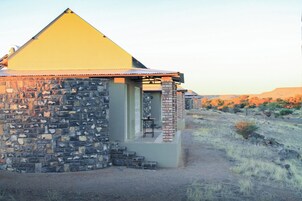 Un edificio de piedra con techo en forma de pirámide, un pequeño porche y vista a un paisaje seco.
