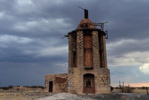 Una torre de ladrillo abandonada con una campana, rodeada por un paisaje árido.