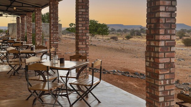 An outdoor dining area with brick pillars, wooden tables, and chairs, overlooking a desert landscape. - Alte Kalkofen Lodge (Simplon)