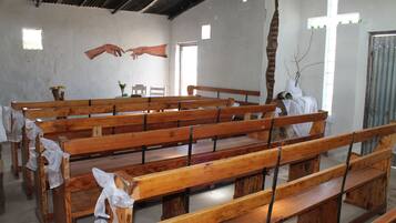 Ein Kircheninneres mit Holzbänken, einem Kruzifix an der Wand und einem Fenster mit Tageslicht.