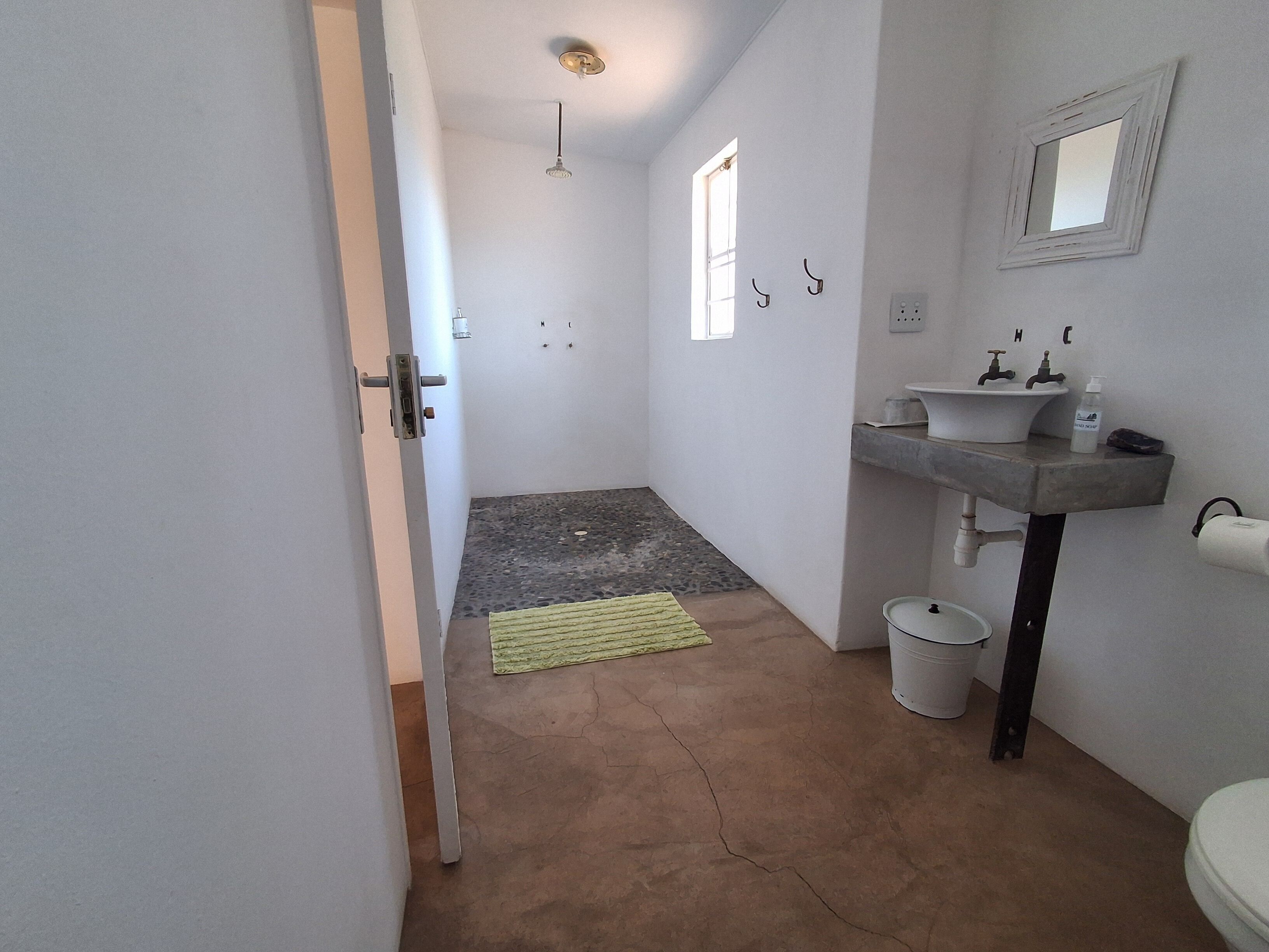 Un baño con lavamanos, espejo y retrete. Hay un perchero y una ventana pequeña.