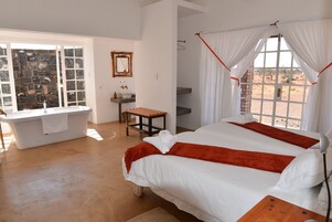 Un dormitorio con una cama grande, un ventanal con cortinas, una bañera y una mesita.