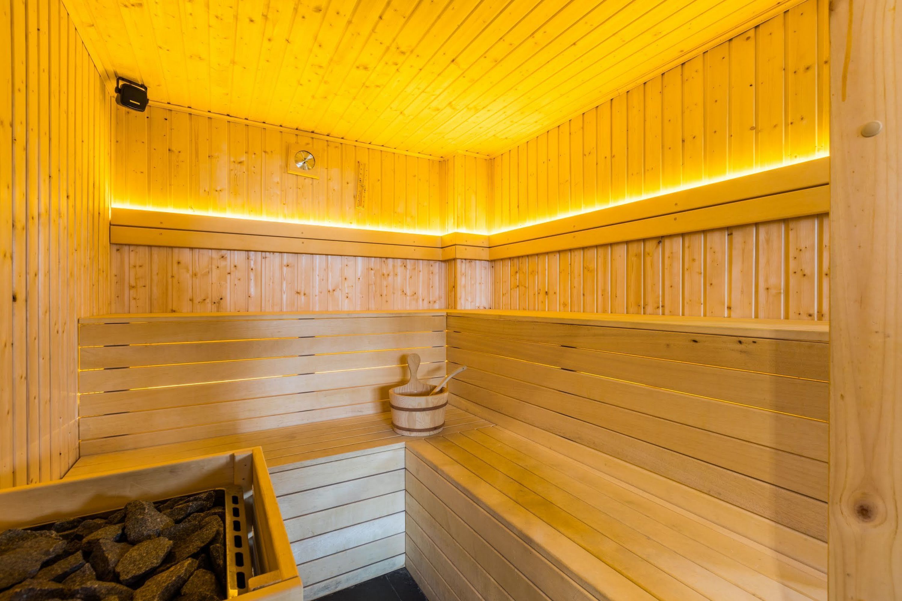A sauna with wooden walls and benches, a small window, and a bucket with a brush.