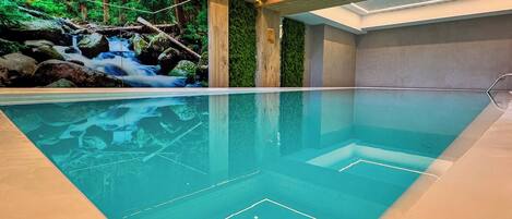 Piscina interior com um mural de cachoeira, painéis de parede de madeira e teto com design de floresta.