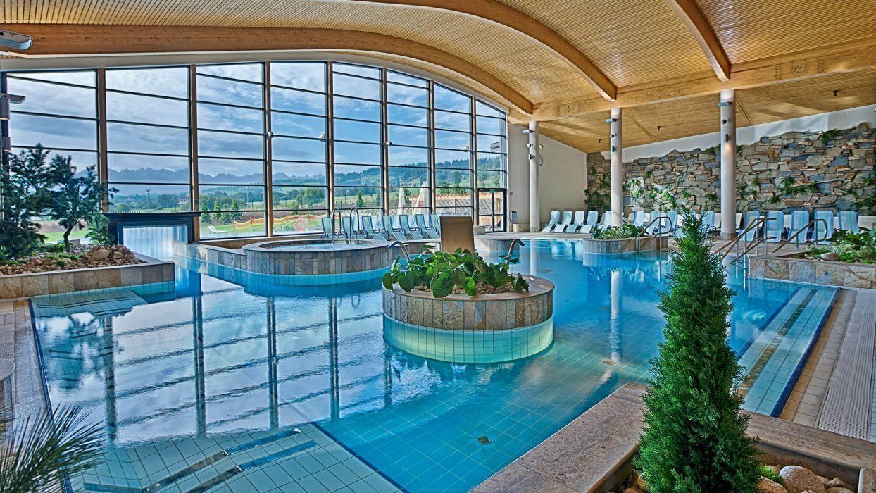 A large indoor swimming pool with multiple lanes, surrounded by lounge chairs and a stone wall.