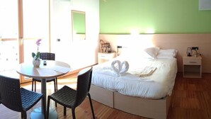 Een kamer met een bed, een ronde tafel met stoelen, een klein bureau en een raam.