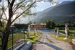 Un chemin bordé de statues menant à un bâtiment à la façade jaune et au toit rouge.