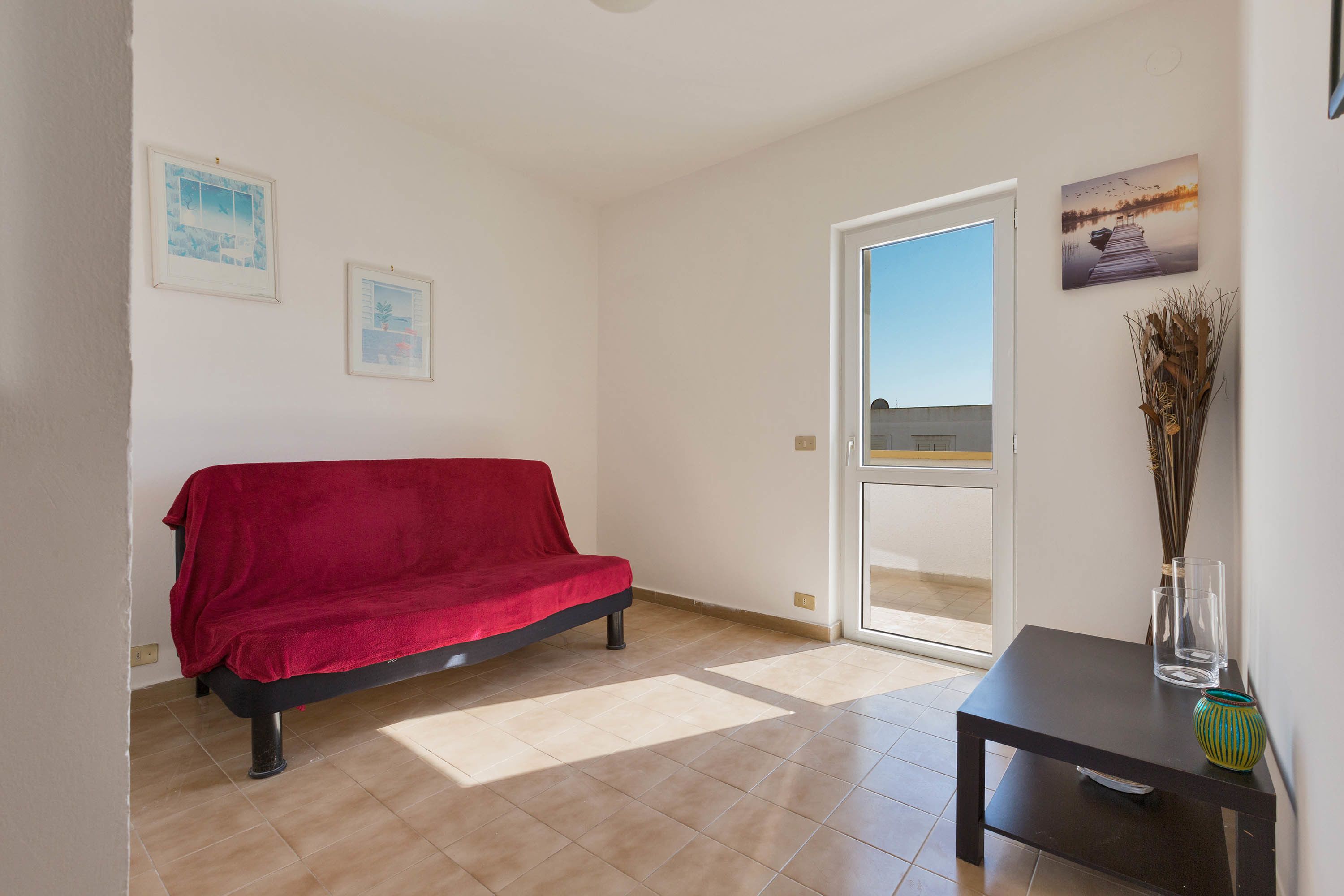 Una habitación con un sofá rojo, una mesita con un florero y dos cuadros en la pared.