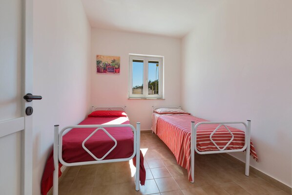 Una habitación pequeña y bien iluminada con dos camas, una ventana y una puerta.