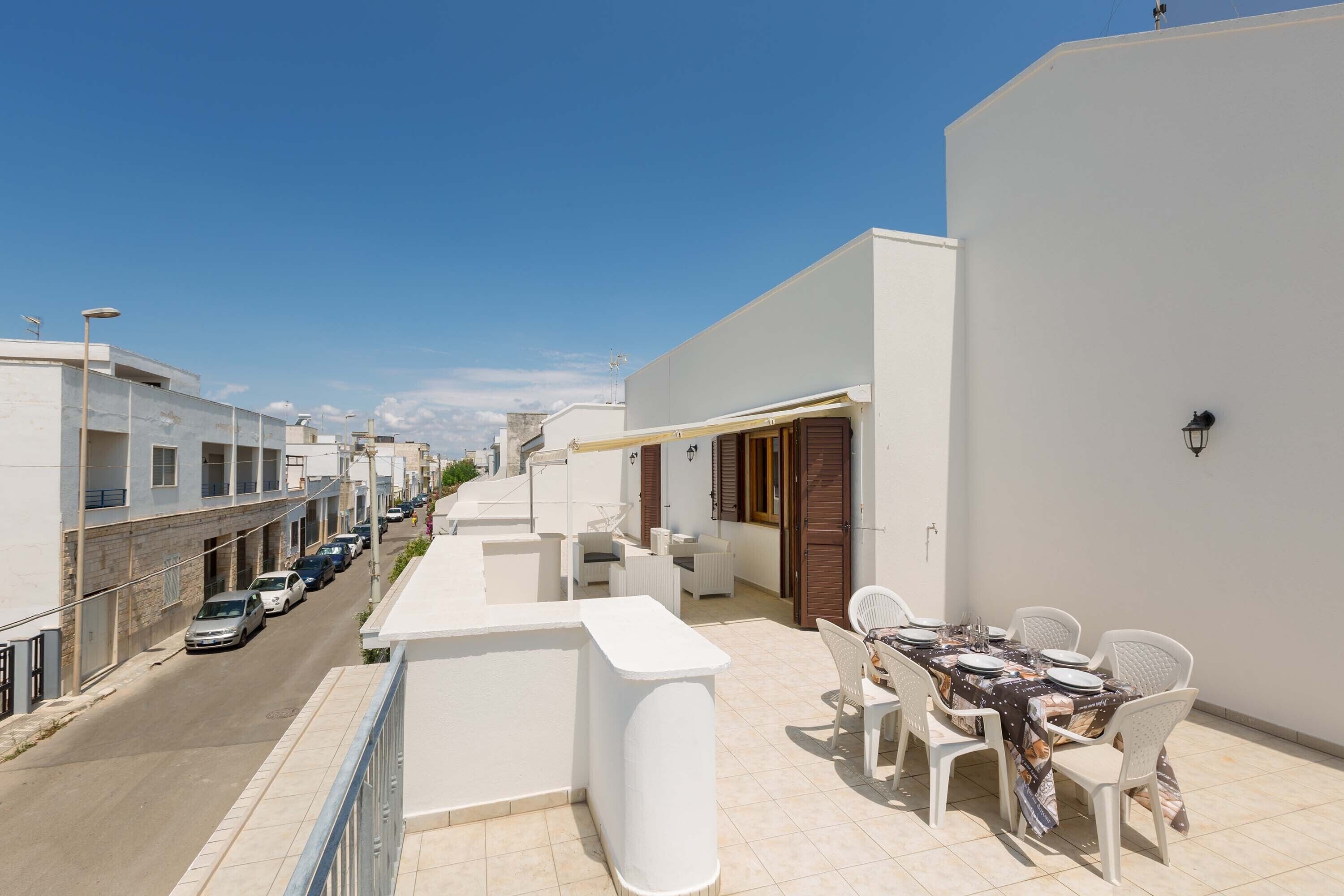 A balcony with a dining table set, white chairs, and a white wall.