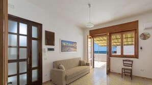 A room with a sofa, a chair, a painting, a clock, and a view of the sea through a window. - 1133 Appartamento Orizzonte by Barbarhouse (Porto Cesareo)