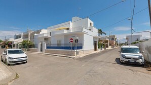 A white building with a blue balcony, a no entry sign, and two parked cars on a clear street. - 1133 Appartamento Orizzonte by Barbarhouse (Porto Cesareo)