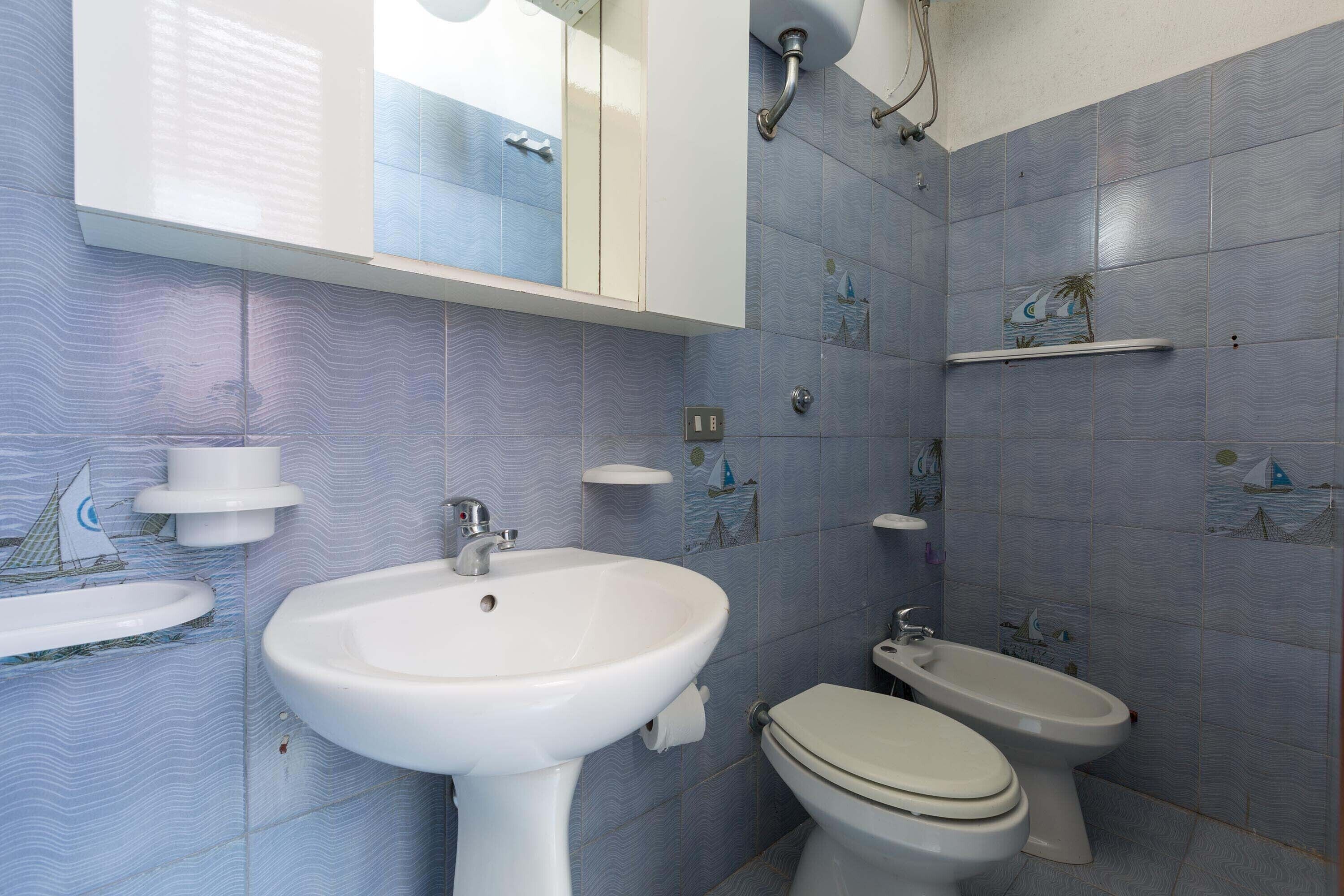 Ein Badezimmer mit weißem Waschbecken, WC und Bidet, dessen Fliesen ein gewelltes Muster zeigen.