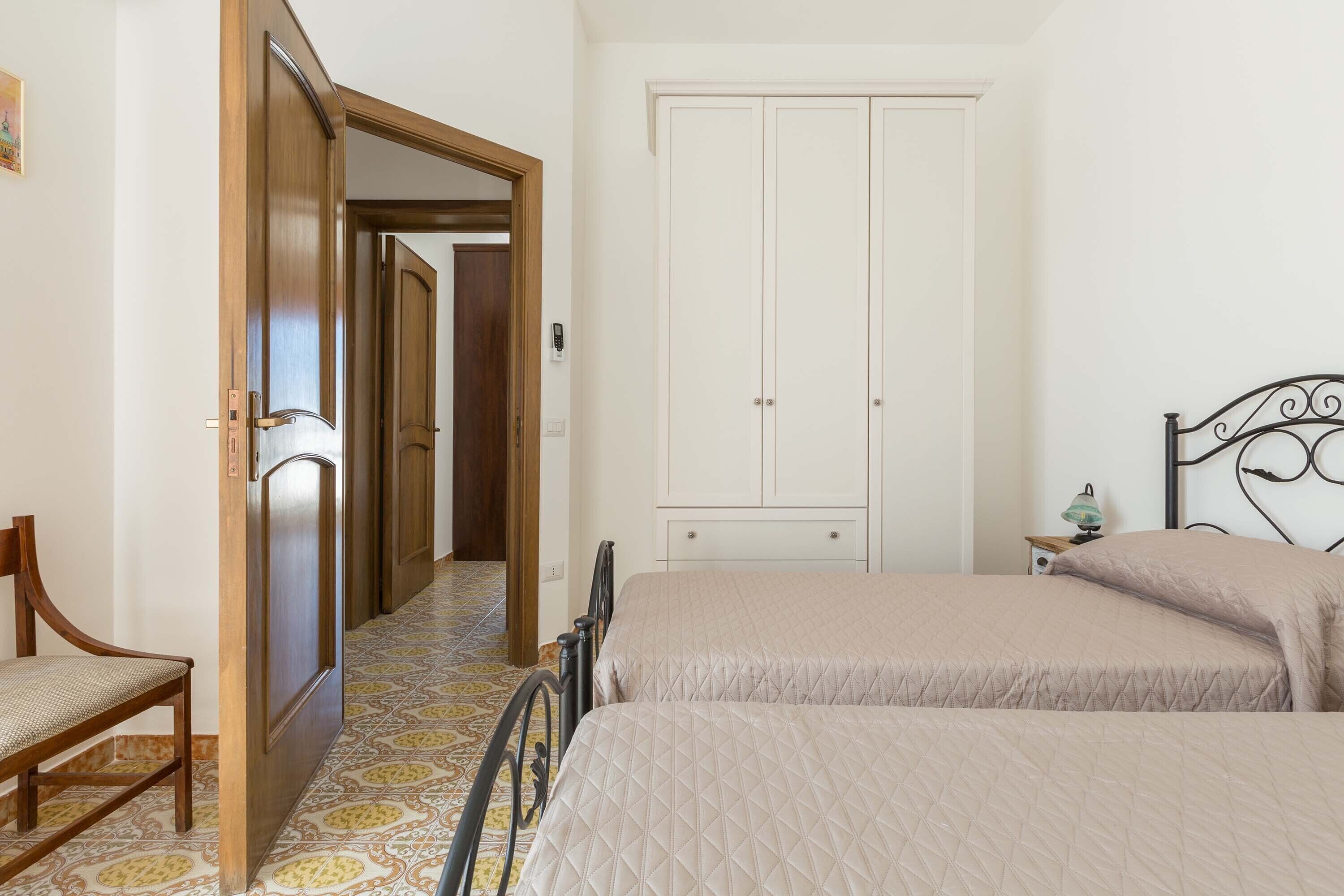A bedroom with two beds, a wooden chair, a wardrobe, and a patterned floor.