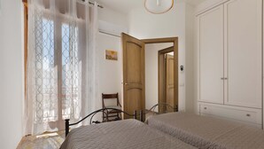 A bedroom with two beds, a wooden door, a chair, and a painting on the wall. - 1133 Appartamento Orizzonte by Barbarhouse (Porto Cesareo)