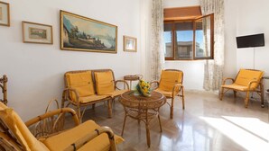 A living room with wicker furniture, a round table with a vase, and a painting on the wall. - Appartamento Sabbia Chiara (Porto Cesareo)