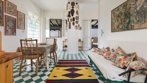 A room with a checkered floor, a sofa with patterned cushions, a dining table with chairs, and various wall decorations including framed pictures and a large painting. - Attico La Baia (Gallipoli)